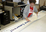 A student employee in Copy & Design Services transfers vinyl lettering onto a banner